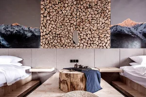 A modern bedroom featuring a log coffee table with a blue blanket, two twin beds with white bedding, and a wall stacked with 