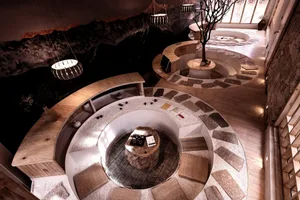 Modern cafeteria interior with circular seating area, wood and stone materials, and natural lighting.