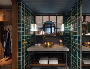 Modern bathroom with green tiled accent wall, white countertop, and brass faucet.