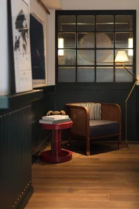 A modern living room featuring a wooden accent table with a red base, a comfortable armchair with a striped cushion, and a fl