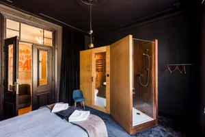 A modern minimalist bedroom with dark interiors, featuring a glass shower enclosure, wooden doors, and neutral color palette.