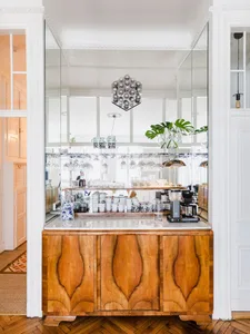 Modern residential kitchen bar with wooden cabinets, glass shelves, and metal appliances.