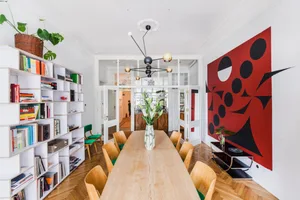 Modern dining room with wooden table and chairs, white walls, and red geometric wall art