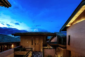 A residential building exterior at night with wooden panels and illuminated stone pathway.