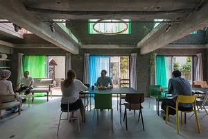 Interior view of a cafe with concrete walls, glass windows, fabric curtains, and green plants.