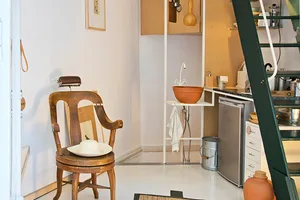 A minimalist kitchen with wooden furniture, a terracotta bowl, and a metal refrigerator.