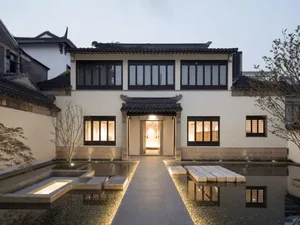 Modern house exterior with stone cladding, multiple windows, and a courtyard.