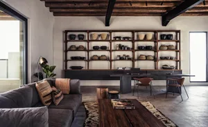 A modern industrial living room featuring wooden shelves, a gray sectional sofa, and a concrete floor.