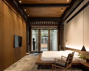 A minimalist bedroom with a wooden bed platform, stone floor, and natural light.
