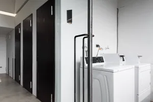 A minimalist laundry room with white appliances and dark wooden doors.
