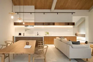 A minimalist living room featuring a wood dining table and chairs, a white sofa, and a modern kitchen area with wooden elemen