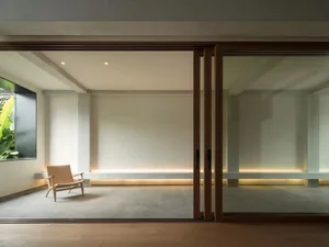 Modern living room featuring concrete flooring and wooden furniture, with large windows and minimalistic design.