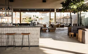 Concrete restaurant bar with stools, exposed brick wall, and outdoor seating area with umbrellas and lounge chairs.