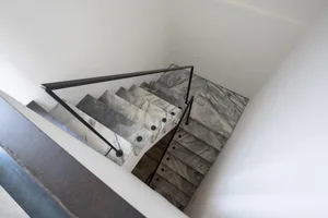 A modern staircase with marble steps and railings, viewed from above in a white-walled room.