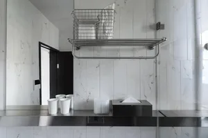 Modern minimalist bathroom with glass tiles, a metal shelf with a wire basket, and a black towel rack.