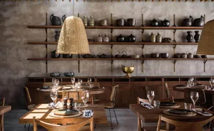 A modern restaurant interior with wooden tables, chairs, and shelves filled with ceramic pottery.