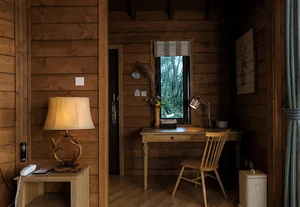 A cozy wooden home office desk with a lamp, chair, and natural light from a window.