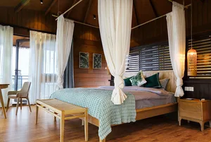 A modern bedroom with a wooden canopy bed, white curtains, and a light wooden bench. The room features a wooden ceiling and w