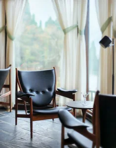 A modern living room featuring a black leather couch, wooden coffee table, and large windows with white curtains.