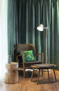 A modern living room with a comfortable chair and ottoman, featuring a palm leaf-patterned pillow and a floor lamp.