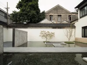 A minimalist water feature with concrete walls and a pond, surrounded by a white wall and greenery.