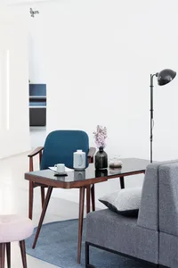 A modern living room featuring a leg table and couch, with a vase of flowers and a lamp.