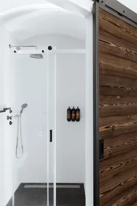 A modern minimalist bathroom features a wood-framed sliding door, a glass shower enclosure, and black tiles on the floor and 
