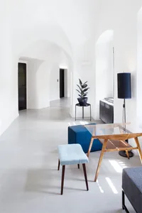 Modern minimalist interior with a concrete floor, blue ottoman, and wooden lamp.