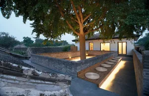 A serene garden area featuring concrete walkways, brick walls, wooden seating, and glass windows.
