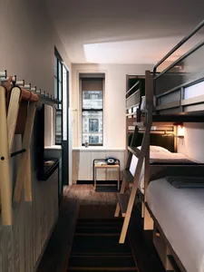 A minimalist bedroom features modern bunk beds made of wood with a ladder, a small table with a retro phone, and a window wit