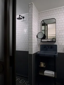 Modern minimalist bathroom with black and white tiled walls and floor, featuring a wall-mounted sink, mirror, and shower head