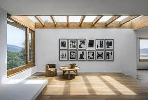 Modern, minimalist living room featuring abstract black-and-white art on a white wall, wooden floors, a rustic stump chair, a