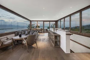 A modern living room with wooden flooring, a glass wall, and comfortable seating.