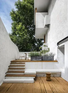Minimalist outdoor space featuring wooden stairs, white benches, concrete walls, and metal planters with greenery.