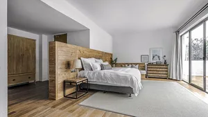 A minimalist bedroom featuring a wooden panel bed, white bedding, and a gray rug on a wooden floor.