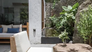 A minimalist garden patio featuring concrete and stone materials with a small water feature and greenery.