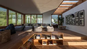 A modern living room with wood flooring, large windows, and comfortable seating areas.