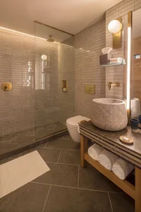 A modern minimalist bathroom with a stone sink, white toilet, and glass shower enclosure.