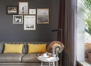A living room with a gray sofa adorned with yellow pillows, situated against a dark gray wall, accompanied by a white side ta