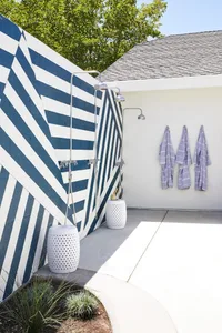 A minimalist outdoor bathroom with a striped concrete wall, two outdoor showers, and hanging towels.