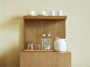 Minimalist office kitchen break room wooden shelf with white mugs, water bottles, and a white kettle.