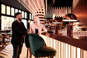A modern bar with metallic black elements, featuring a smiling man and a woman sitting at the counter.