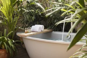 A modern bathroom featuring a white bathtub on a wooden shelf surrounded by plants.
