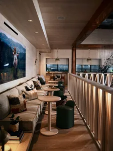 A modern cafe featuring wooden elements, fabric seating, and leather stools.