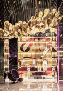 A modern hotel lobby adorned with metallic plates hanging from the ceiling and a curved glass wall.