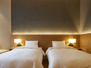 Two neatly made twin beds in a minimalist hotel room with warm lighting and wooden headboards.