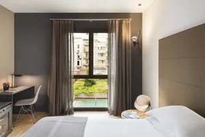 A modern hotel room with textured cotton blend materials, featuring a king-sized bed, desk, and large window overlooking a ga
