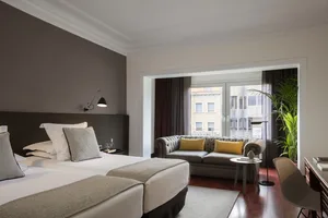 Modern, minimalist hotel suite with grey decor, featuring a comfortable seating area, a large bed with plush bedding, and a s