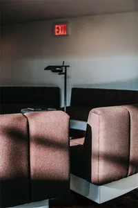 A modern interior featuring cozy fabric sofas with a sleek lamp and an illuminated exit sign.