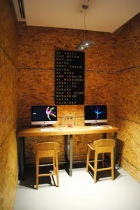A modern, minimalist interior workspace featuring a wooden table with two computers and stools.